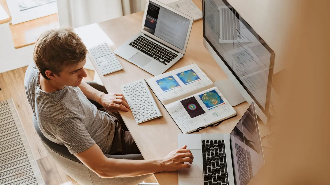 Person working at a desk with a desktop monitor and two laptops