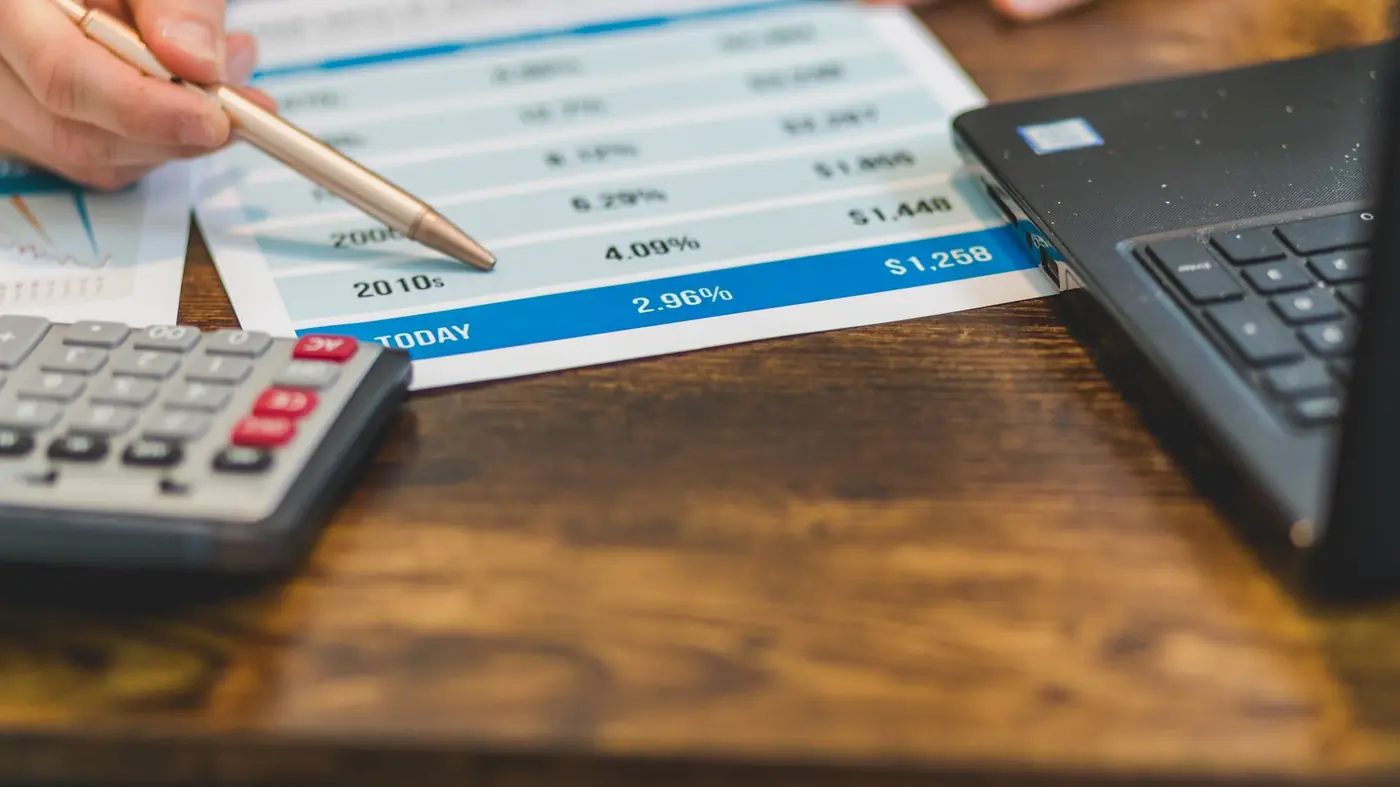 Pen pointing at figures on a printed statement next to a calculator and laptop