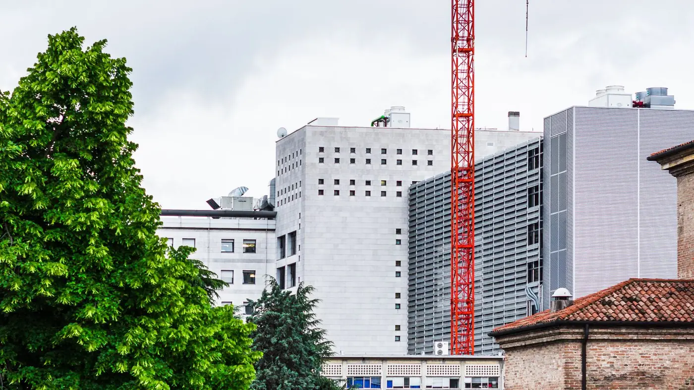 Red tower crane beside office buildings under a cloudy sky