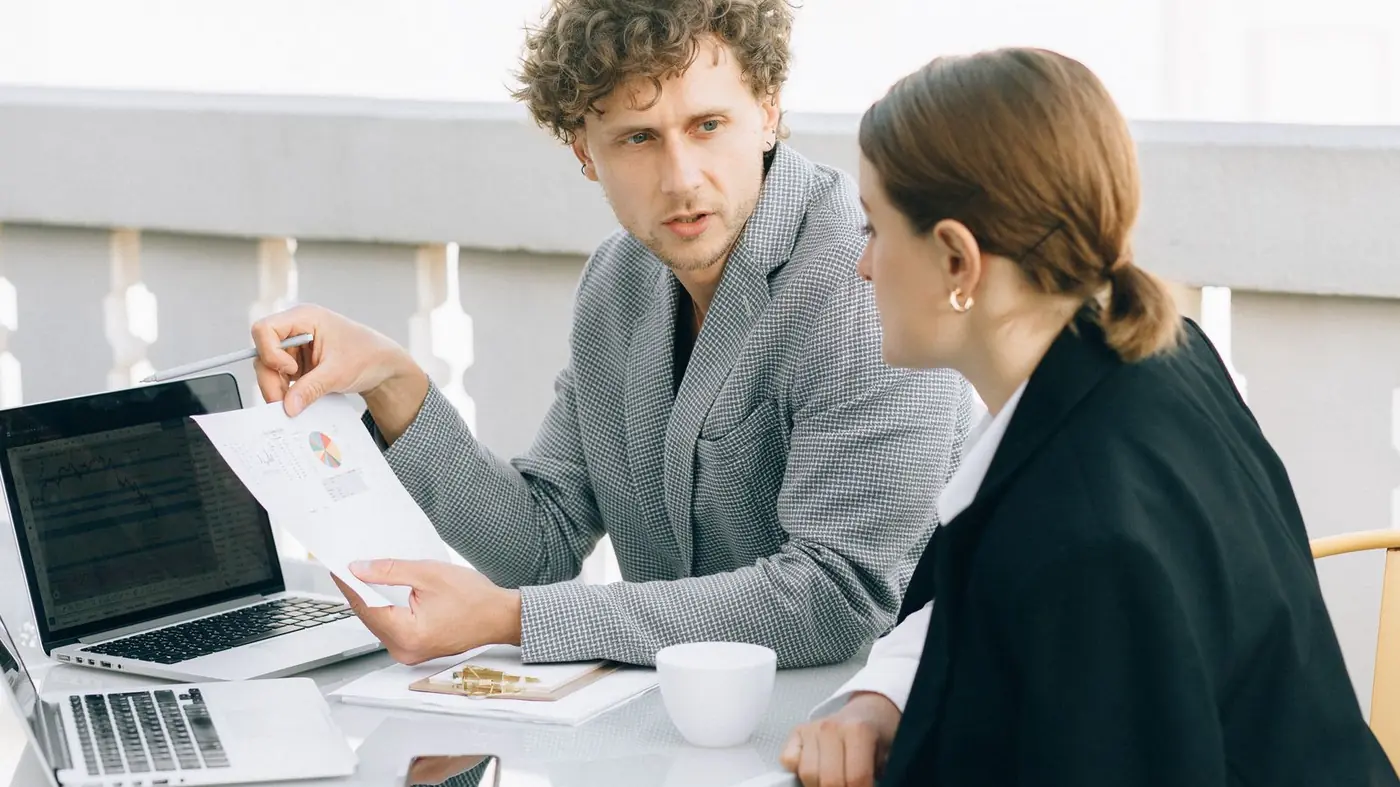 Two colleagues discussing a document beside a laptop
